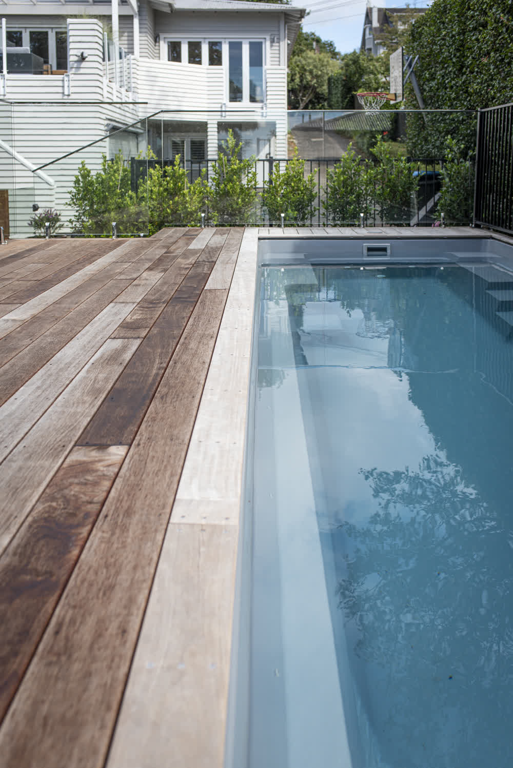 Narrow pool with wooden decking and glass balustrade
